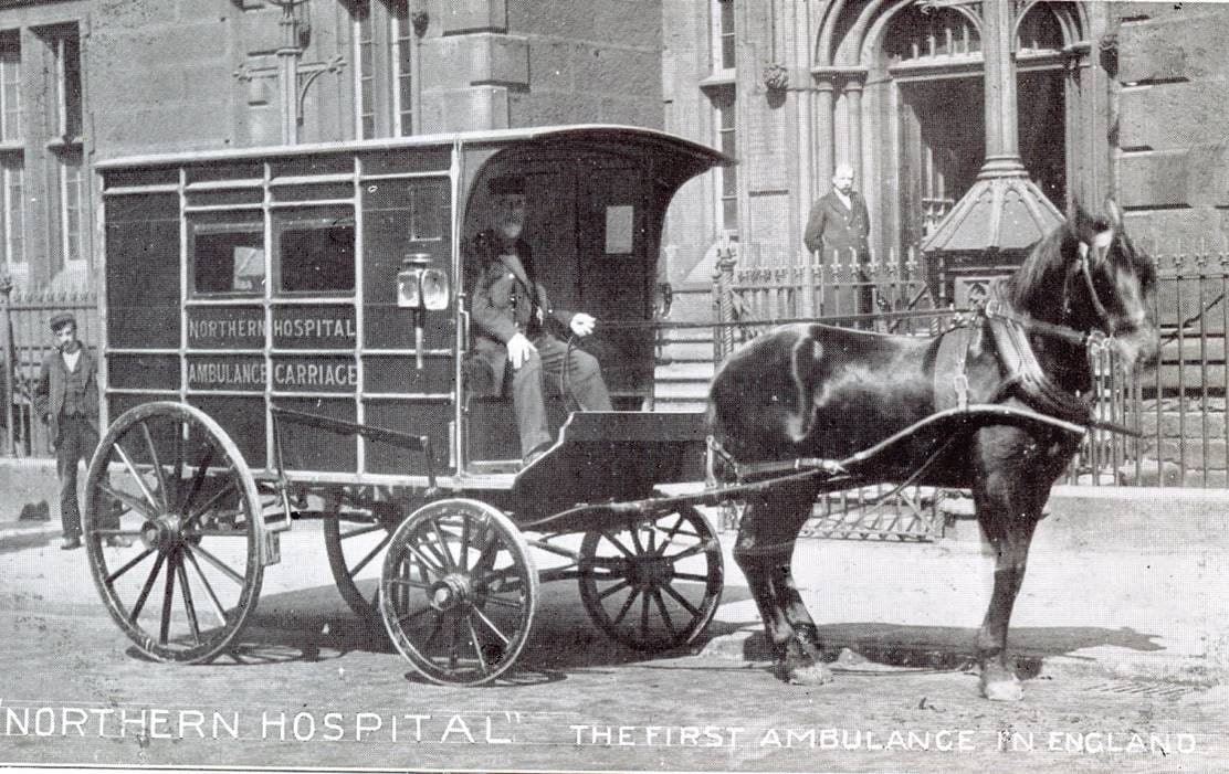 Black-and-white photograph showing a horse-drawn ambulance carriage outside the Northern Hospital, illustrating early emergency medical transport in England