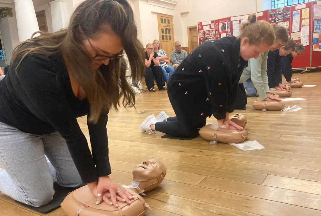People practising CPR chest compressions on manikins during a first aid session