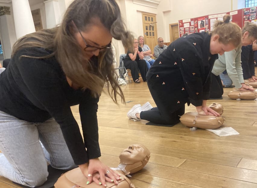 Group of adults practising hands-only CPR on training manikins during a community CPR session.