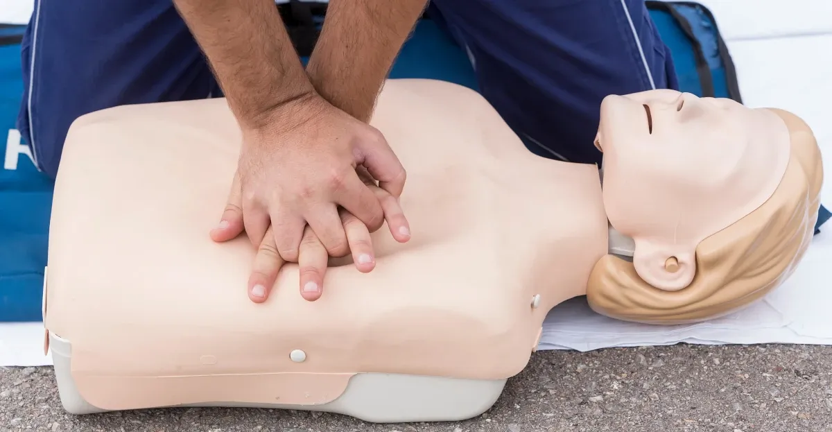 Hands performing chest compressions on a CPR training manikin.