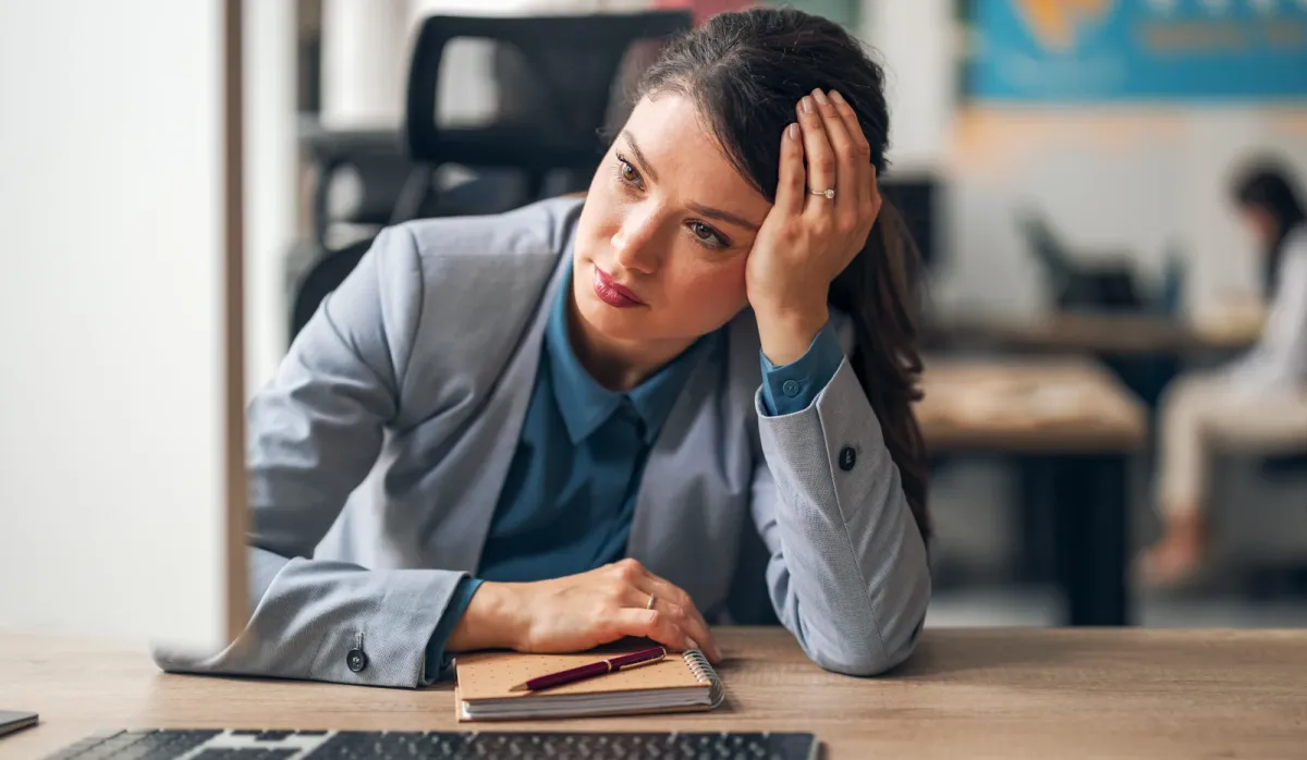 Office worker leaning on one hand at her desk, looking stressed in a workplace setting