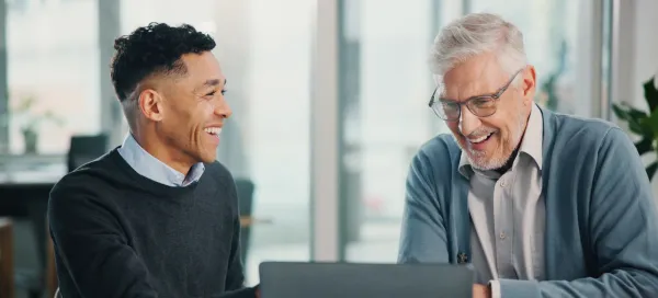 Two colleagues smiling during a conversation at a laptop in a bright office.