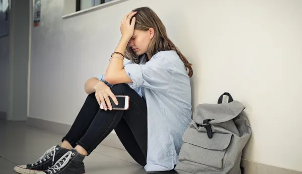 Teenage student sitting on the floor with a severe headache beside a backpack